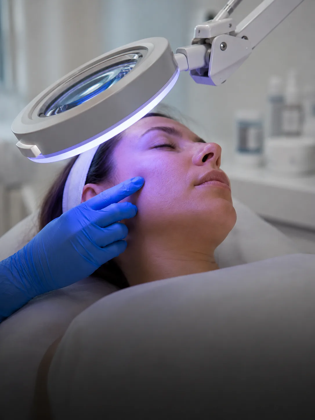 Dermatóloga examinando la piel del rostro de una paciente con lámpara de aumento